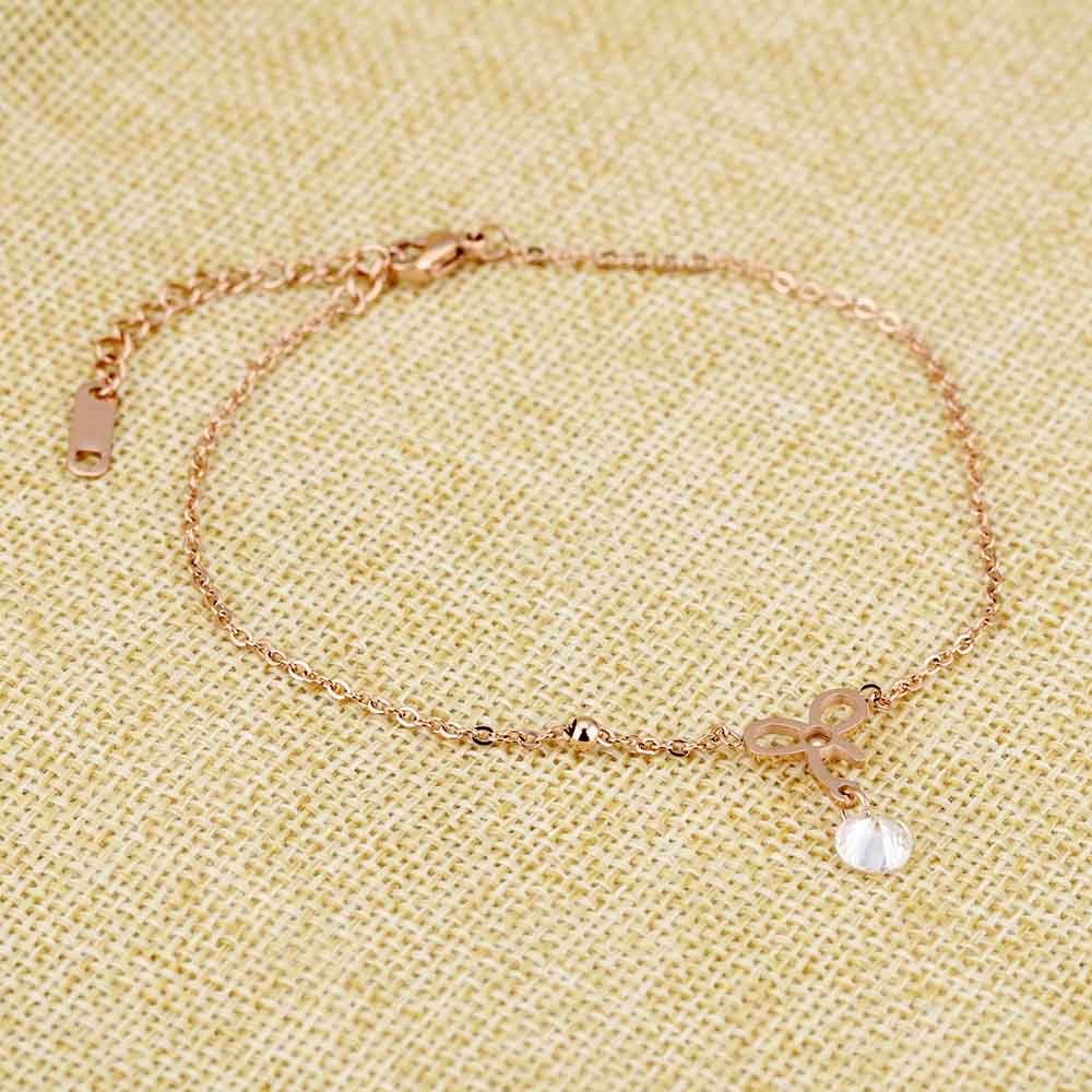 a gold anklet with a sparkling diamond and a studded bow on a textured surface