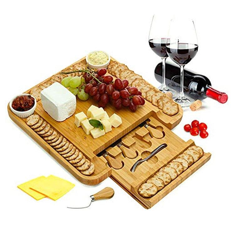 A natural wood serving cheese board with food and bottles of wine besides
