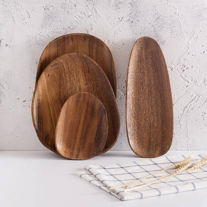 Four irregular acacia wood serving trays in front of a white wall