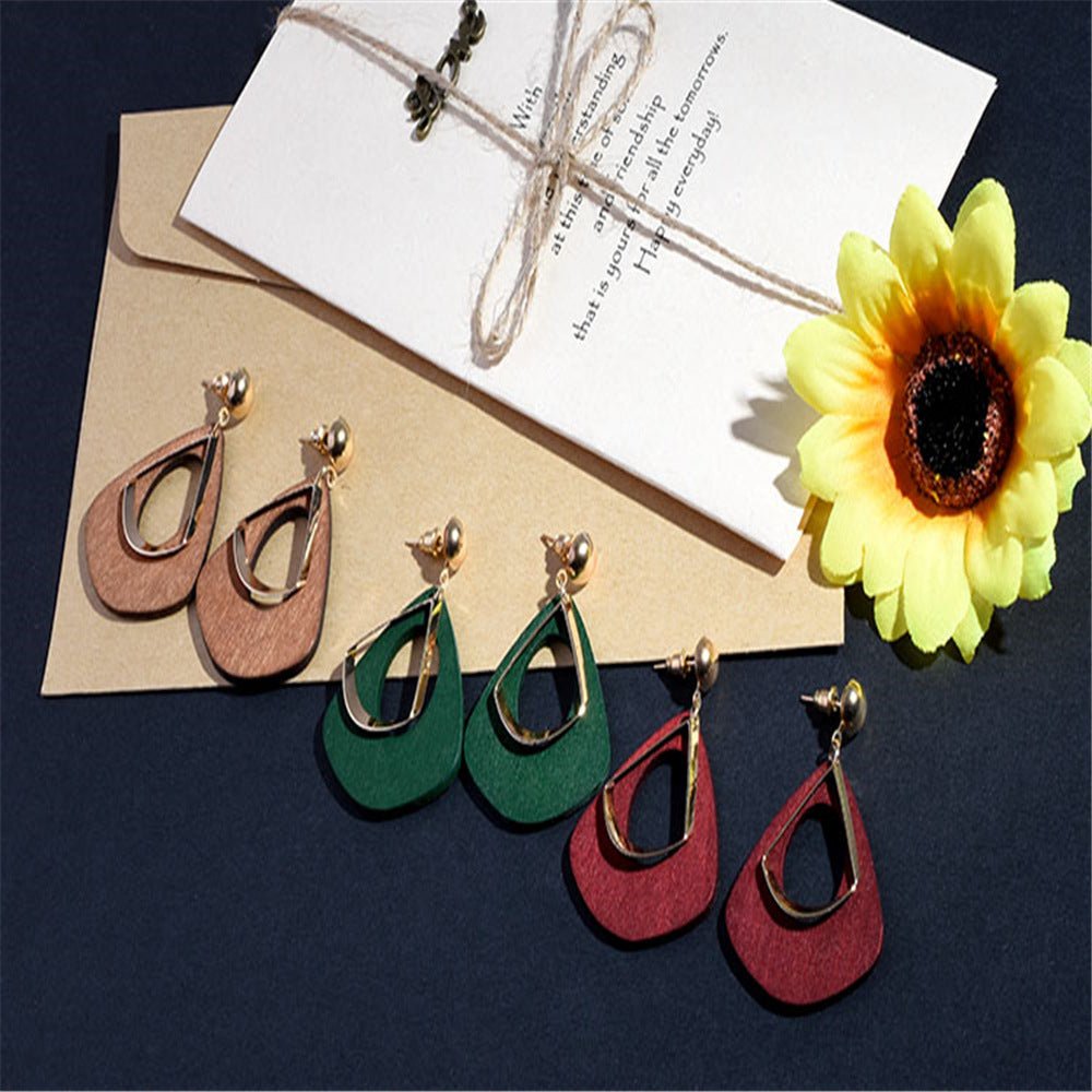 Three pairs of wooden earrings on a table with a flower and an envelope