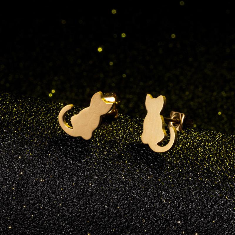 A pair of gold cat earrings on a black canvas and gold glitter