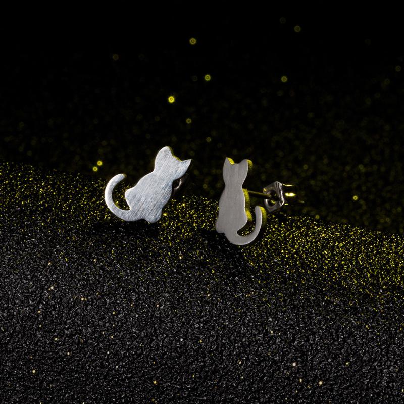 A pair of silver cat earrings on a black canvas and gold glitter