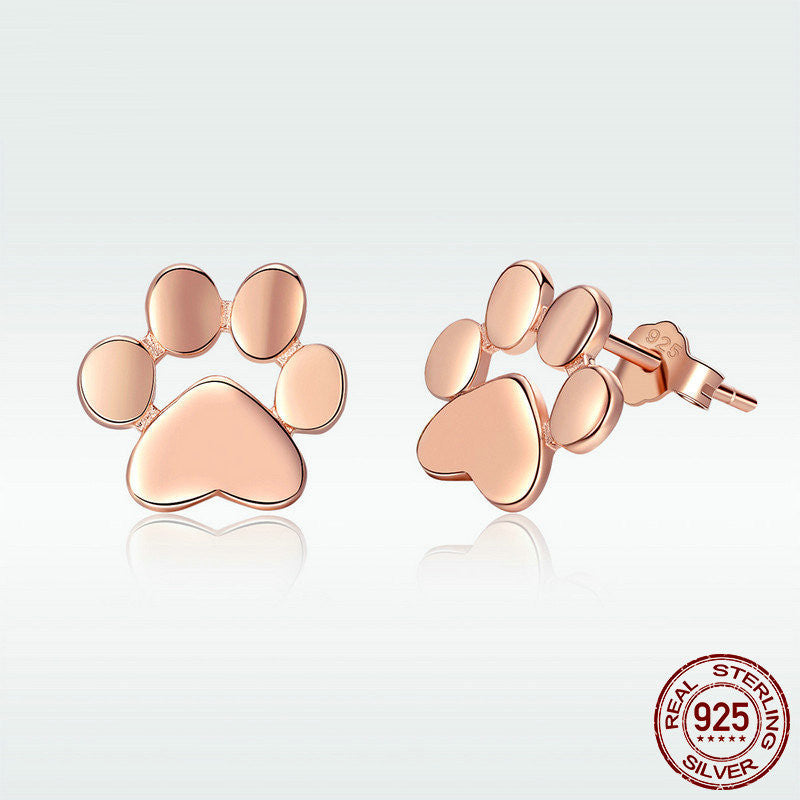 A pair of gold ros dog paws earrings  on a white canvas