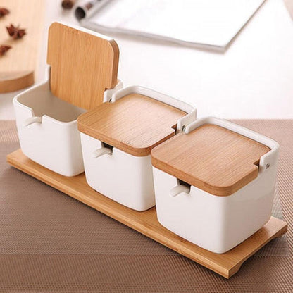 A trio of bamboo and wood clamshell ceramic seasoning jars with wooden lids arranged on a table