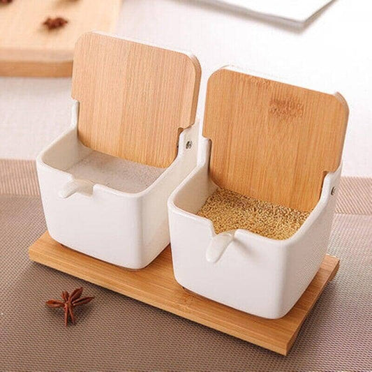 Two bamboo and wood clamshell ceramic seasoning jars with wooden handles displayed on a table