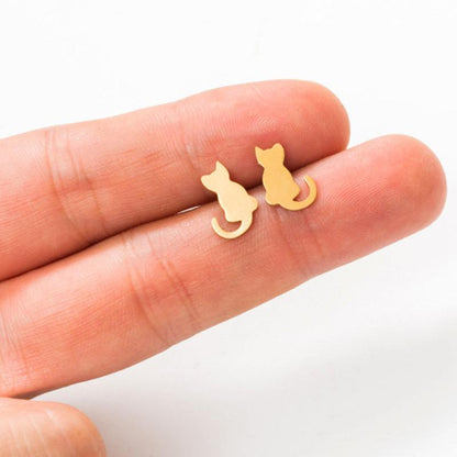 A pair of gold cat earrings hold by 2 human fingers