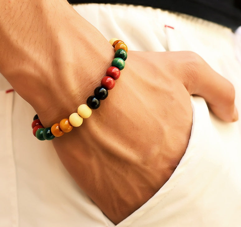 Someone wearing  a multicolored wooden bracelet and white jeans