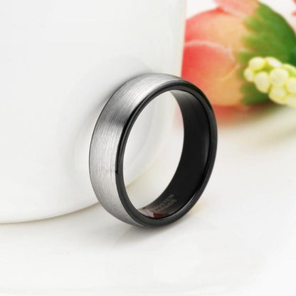 a tungsten ring with a finish silver color over a white table and beside a flower