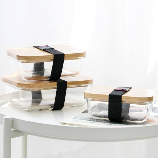 eco-conscious glass food containers with a bamboo lid and an elastic band on a white table
