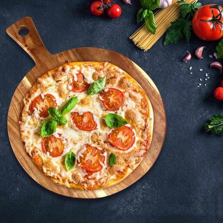 A pizza served on a round acacia wood pizza board over a black countertop