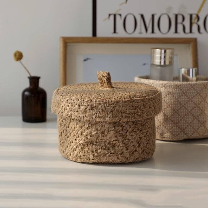 a light brown storage backet made of line and jute with a wheat leaf pattern on a table