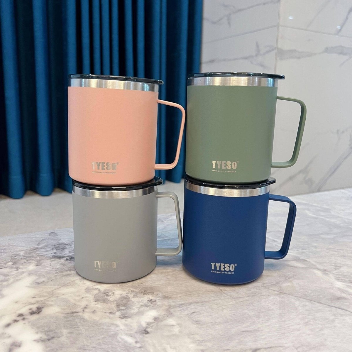 four stainless steel mugs in four different colors over marble countertop